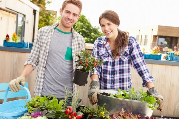 A young man and a young woman smile into the camera as they stand by their garden's harvest.